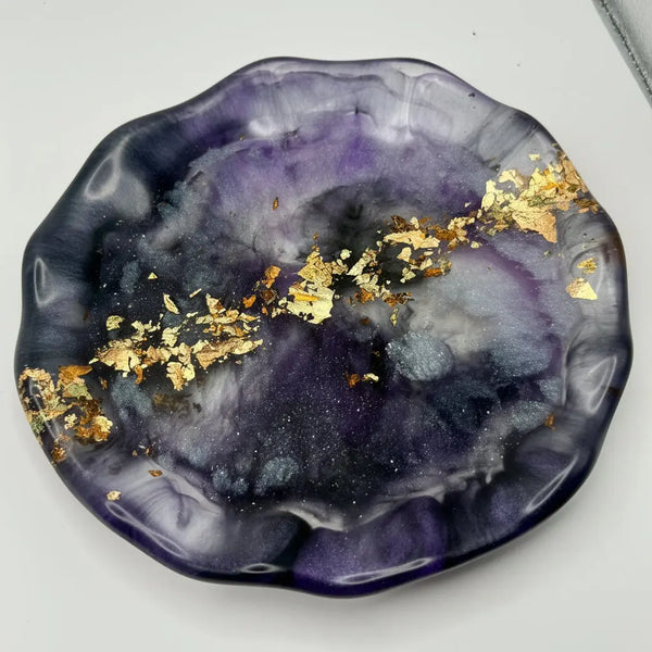 Decorative plate with purple and black marbled design and gold flakes on a white background