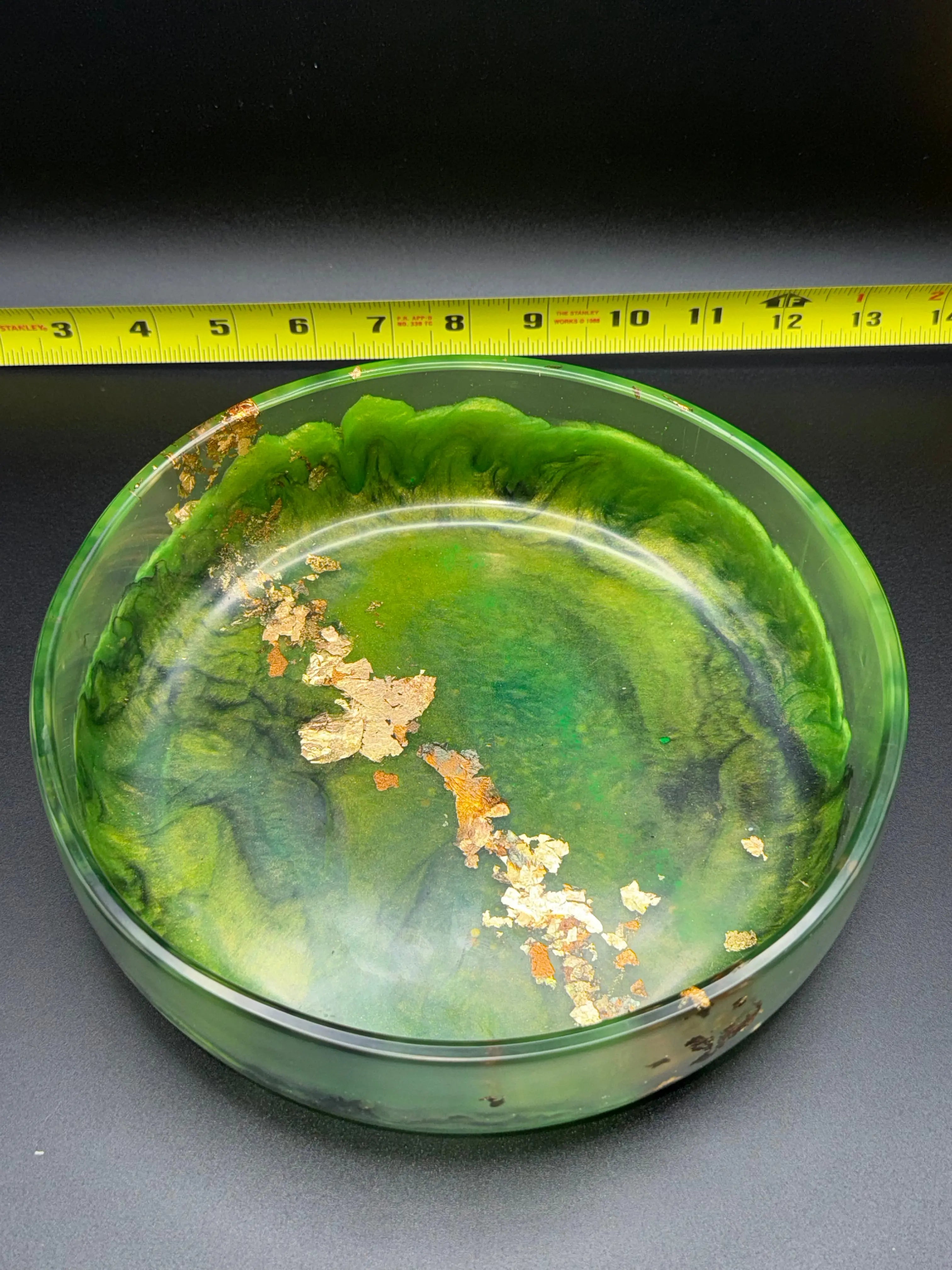 Green and black bowl with marbled design on a dark surface, measured by a yellow tape measure. 8.25 in diameter