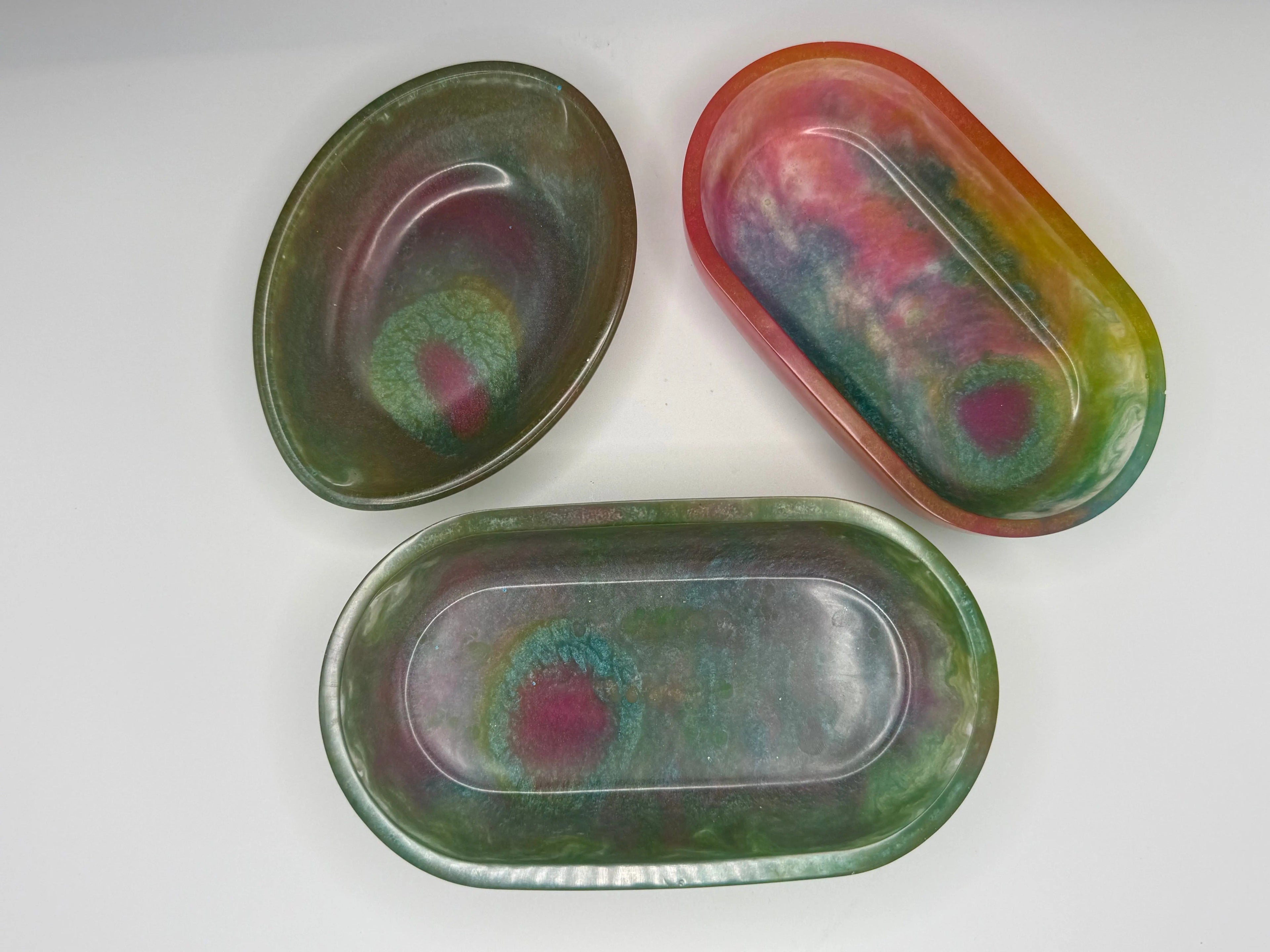 Three oval soap dishes or trinket trays with multicolored colors on a white background. 
